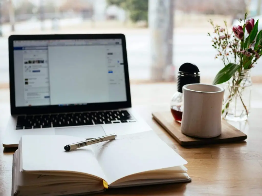 Workspace with laptop, open notebook, pen, coffee mug.