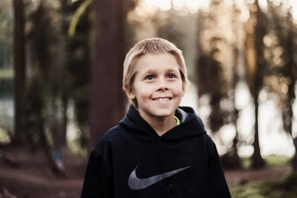 Smiling boy in forest, wearing hoodie.