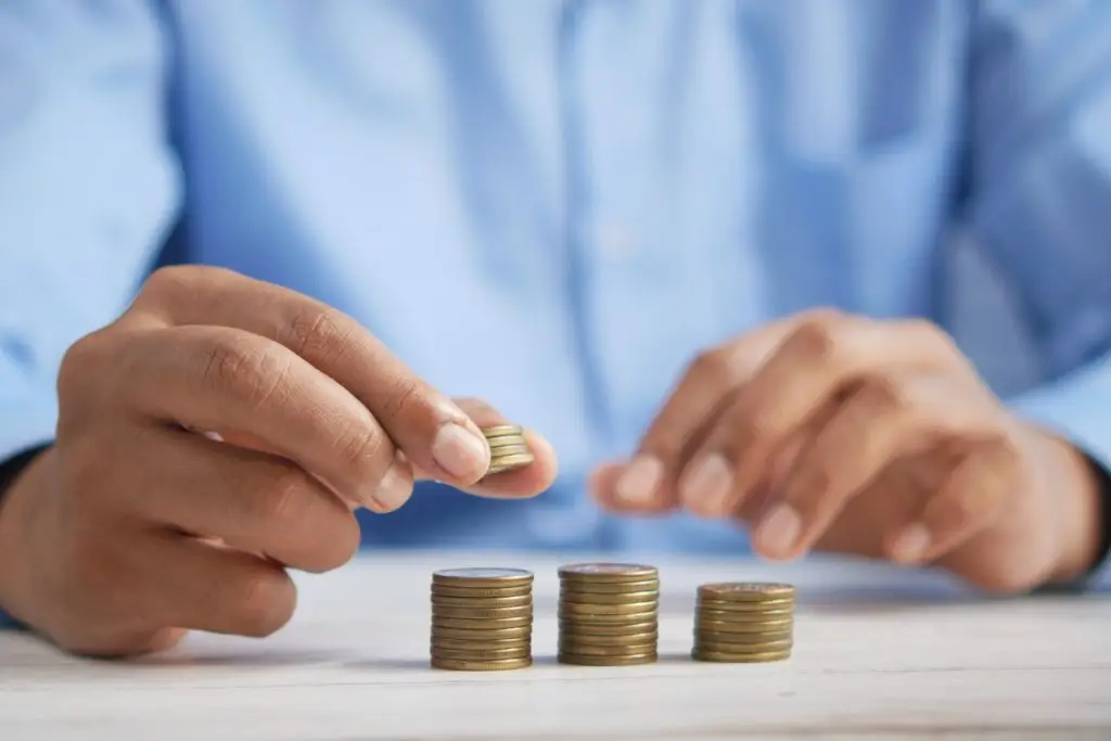 Person counting stacked coins on table.