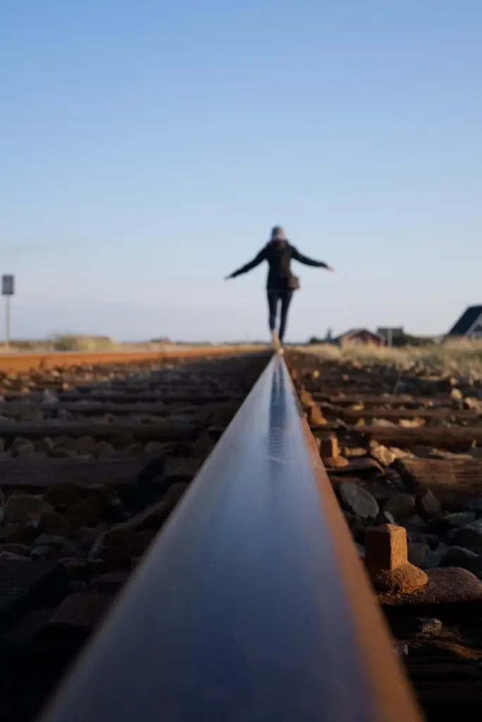 Person balancing on railway track, clear sky background.