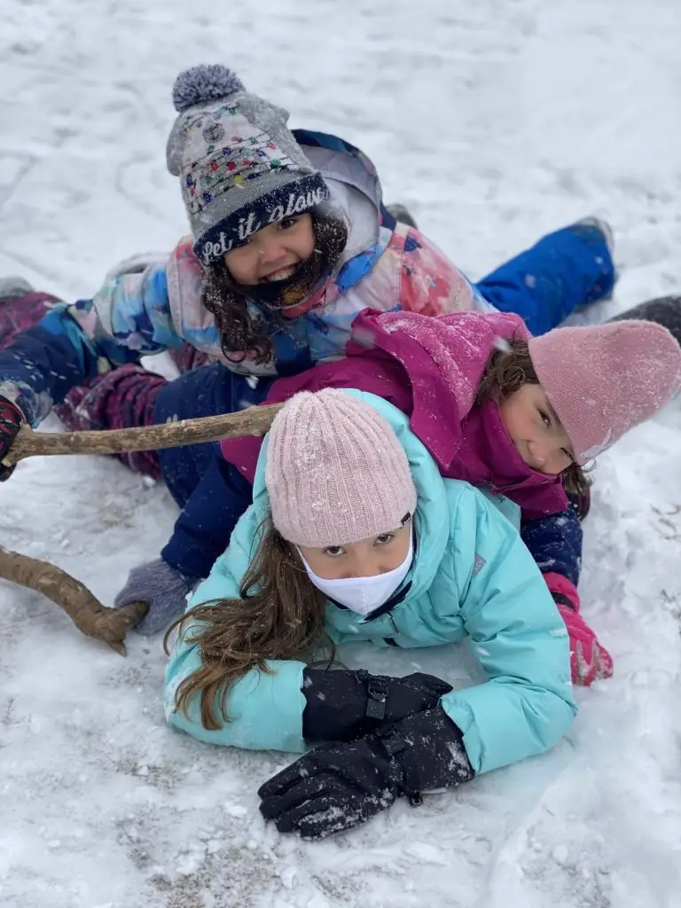 Children play in snow wearing winter clothing.