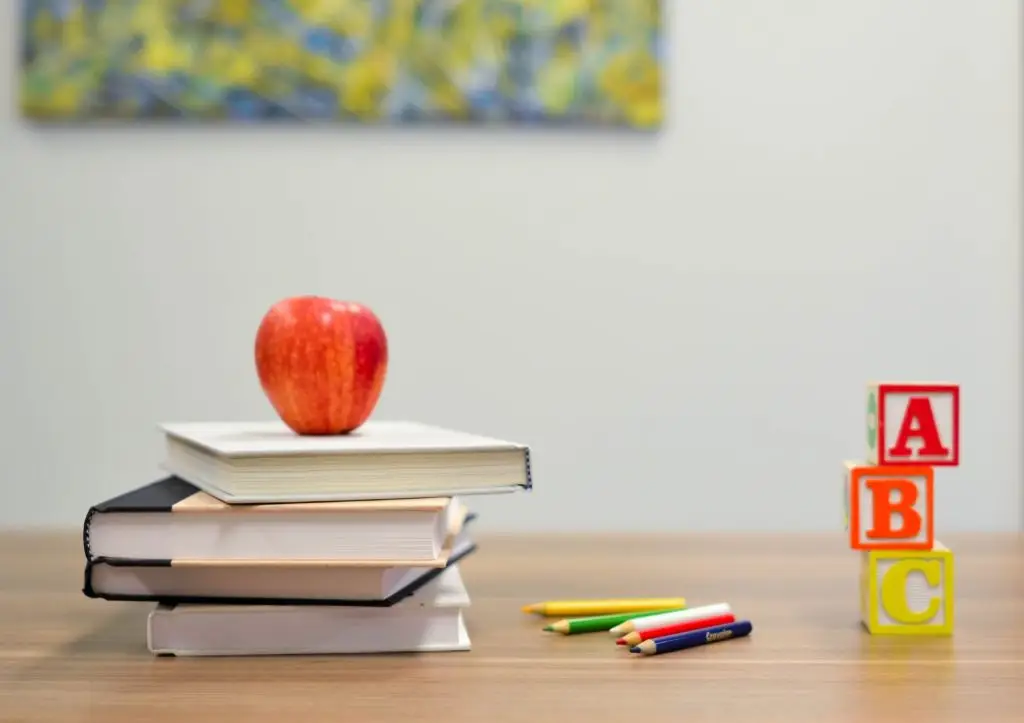 Apple on books with pencils and ABC blocks.