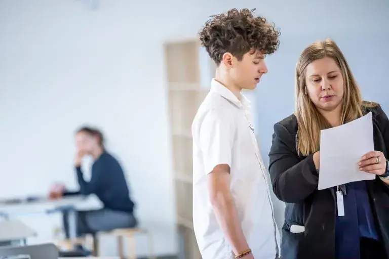 Teacher discussing paper with student in classroom.